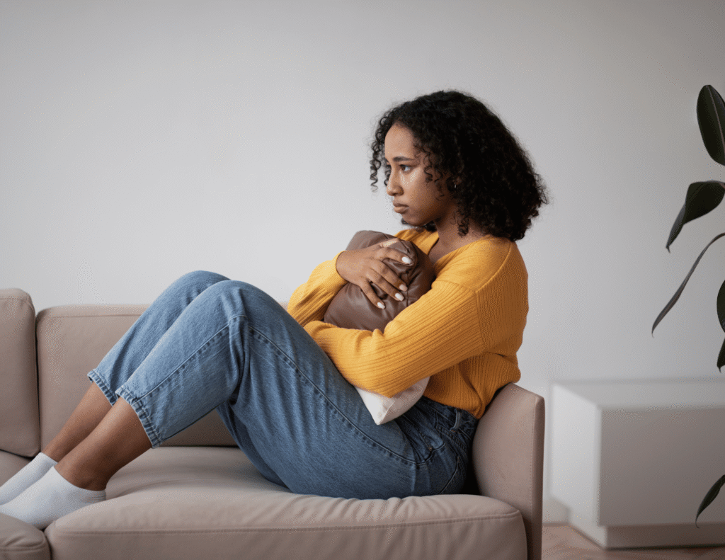 Amazing sides of depression a young Black woman sitting alone on a couch hugging a pillow with a distant expression on her face