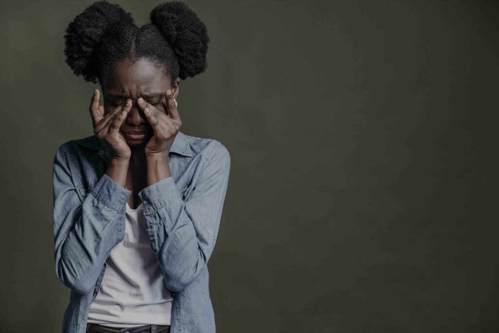 Young Black girl covering her face, head bowed, representing anxiety and the emotional burden of being the oldest daughter