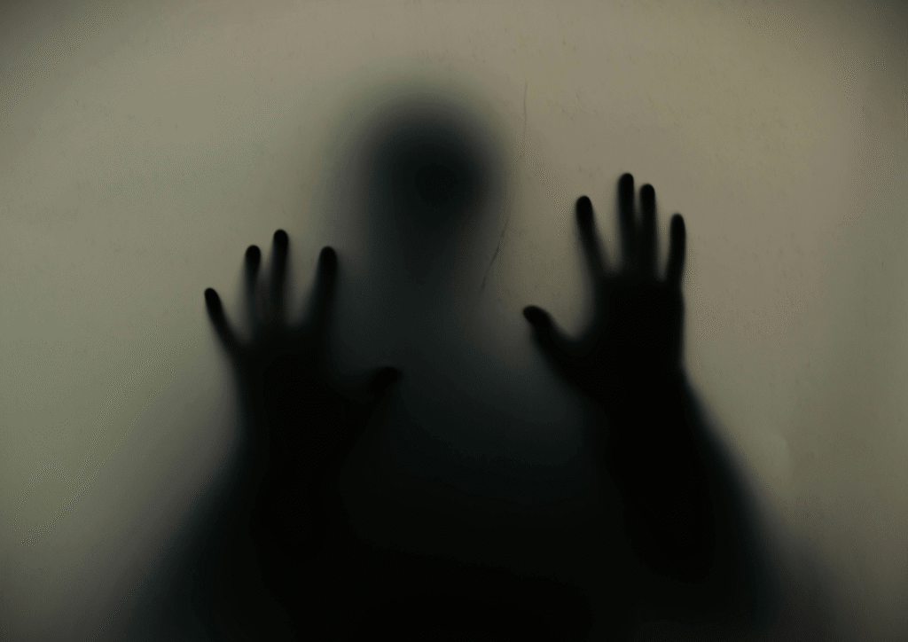 Person behind glass with hands pressed against it, representing isolation and invisibility of those with mental health challenges in Nigeria.