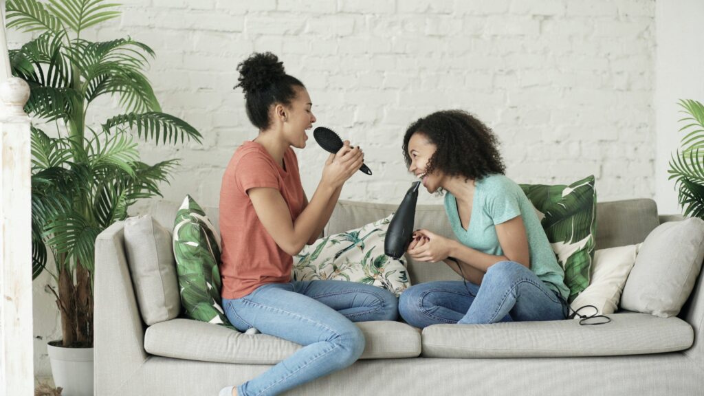 Two friends laughing and spending time together indoors, reconnecting after a long time apart.