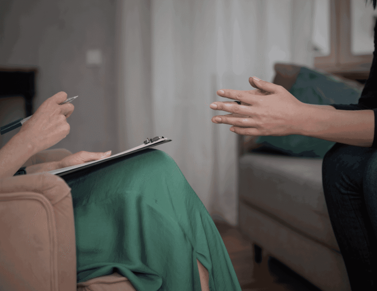 A client speaking to a mental health counsellor during a counselling session while the therapist takes notes on a clipboard