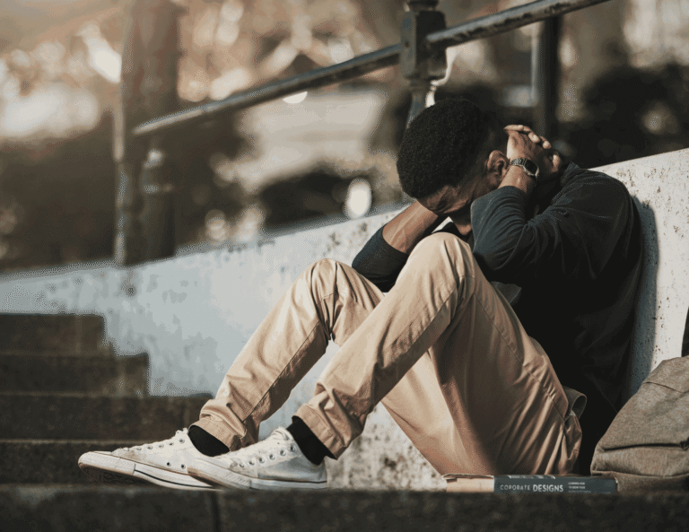Young Nigerian man sitting alone on outdoor steps looking distressed while hiding emotional pain behind silence