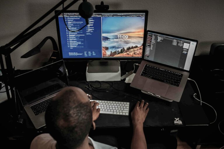 Person working at a desk with multiple monitors and laptops, surrounded by recording equipment, symbolizing content creation workload and mental exhaustion.