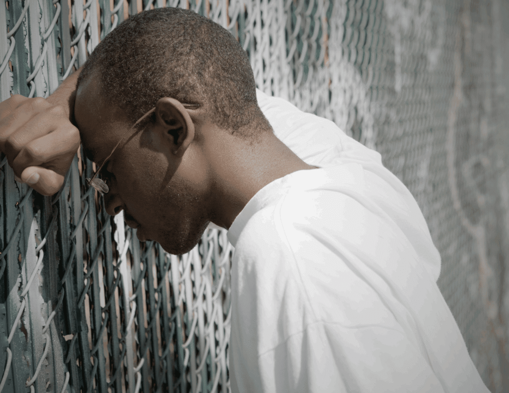 Young Nigerian man leaning against a fence looking stressed while hiding emotional struggles