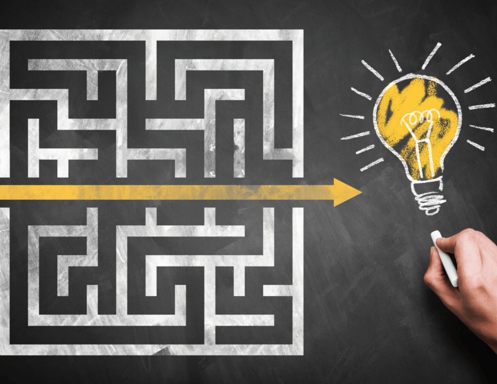 A chalk-drawn maze on a blackboard with a yellow arrow cutting straight through the middle, pointing toward a glowing yellow lightbulb drawn on the right side