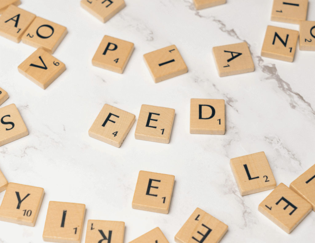Scattered wooden Scrabble letter tiles arranged loosely on a white marble surface, showing various letters including F, E, D, Y, and others