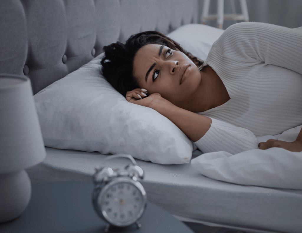 Young woman lying awake in bed at night, staring at the ceiling, unable to rest due to productivity guilt