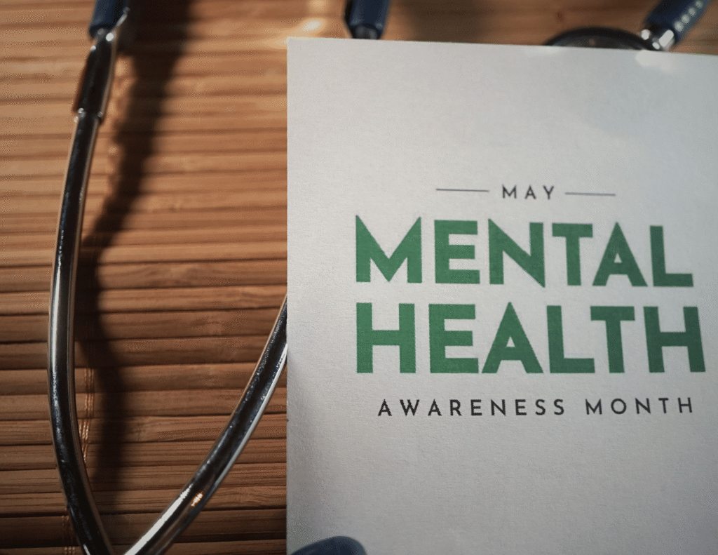 A May Mental Health Awareness Month card with bold green text placed next to a stethoscope on a wooden surface