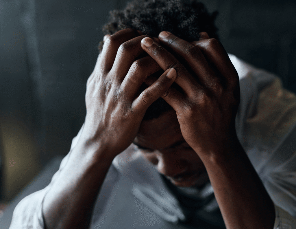A Black man sitting with his head in his hands representing the reality of men's mental health in Africa
